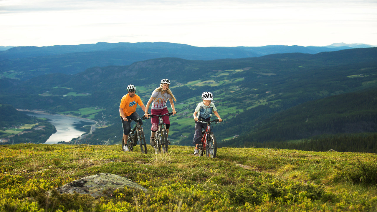 Mann, gutt og jente sykler på toppen av et lite fjell