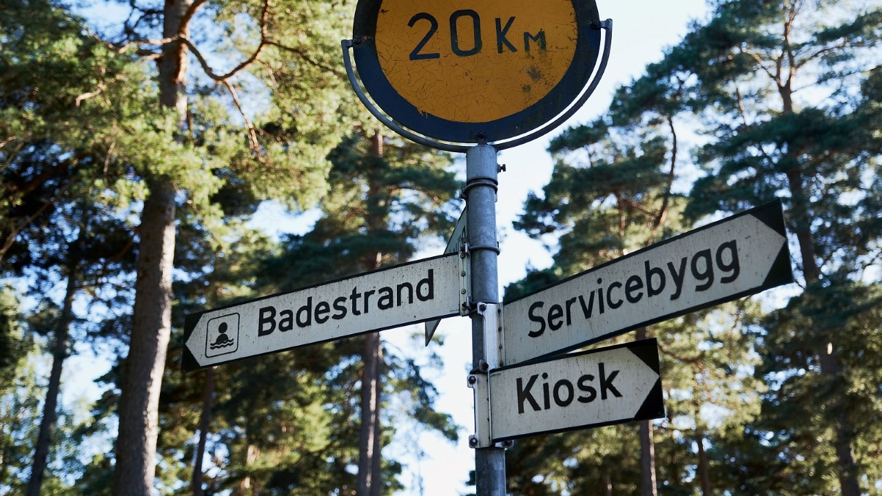 skult som viser vei til badestrand, servicebygg og kiosk. Foto.