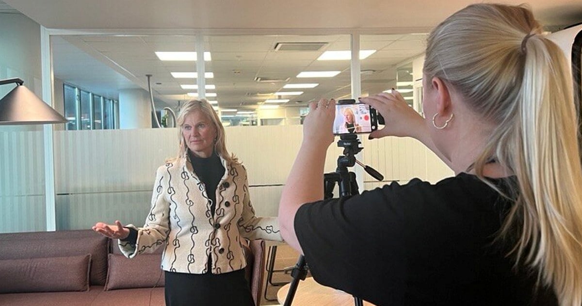 En person med langt lyst hår betjener et mobilkamera som er rettet mot Kristin Krohn Devold. Bak Krohn Devold sees et kontorlokale.