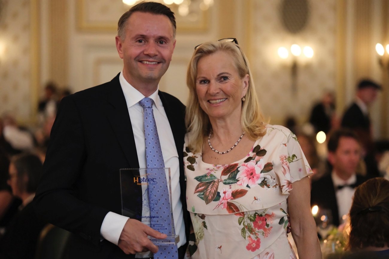 En mann og en kvinne som smiler strålende. Mannen hoder et glass-trofé med teksten Hotrec award inngravert med gullbokstaver.