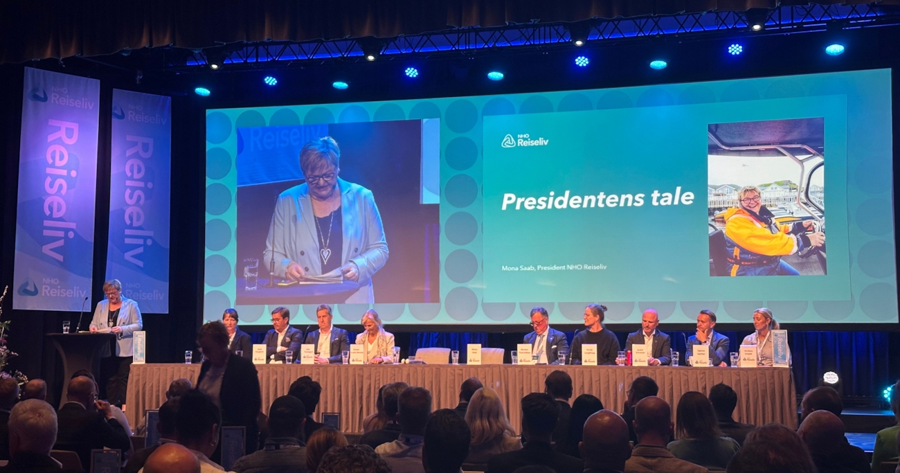 Mona Saab, president i NHO Reiseliv, holder åpningstale under årskonferansen 2025. Hun står ved talerstolen, mens en stor skjerm bak viser både henne og tittelen 'Presidentens tale'