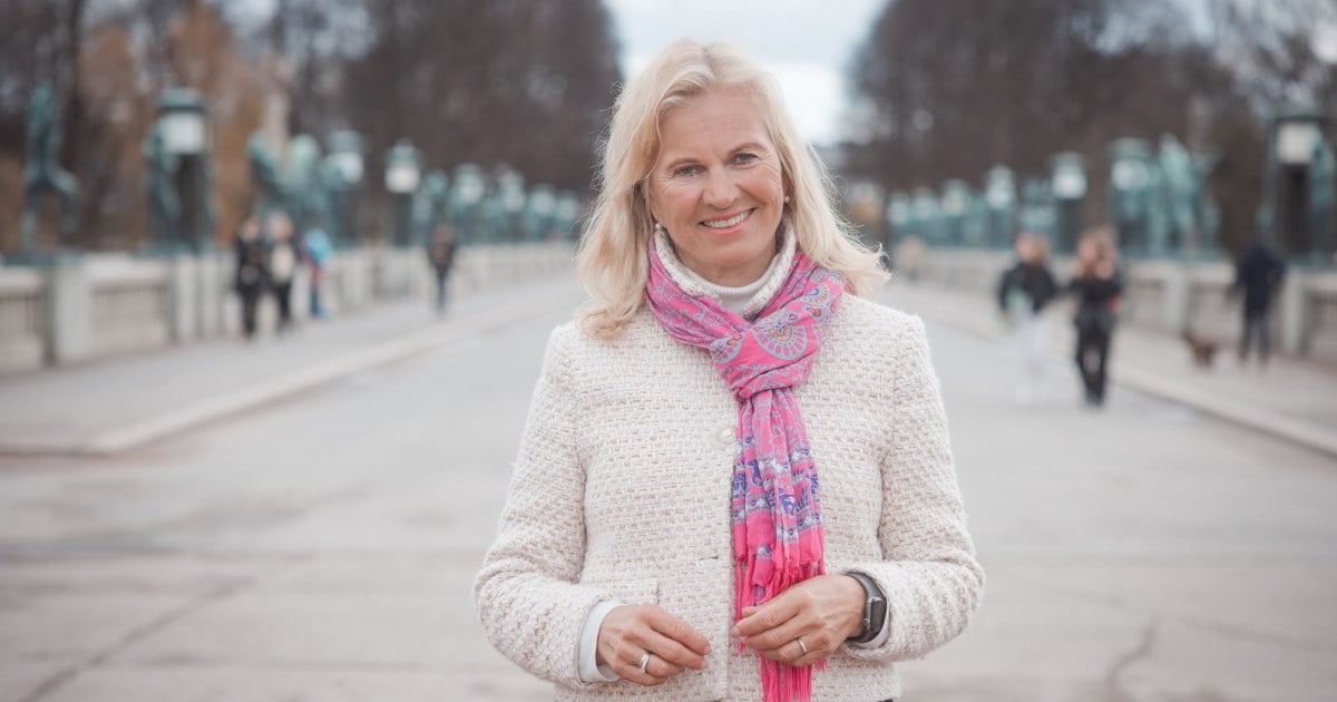 En kvinne i lys jakke og rosa skjerf som smiler mot kamera. Foto.