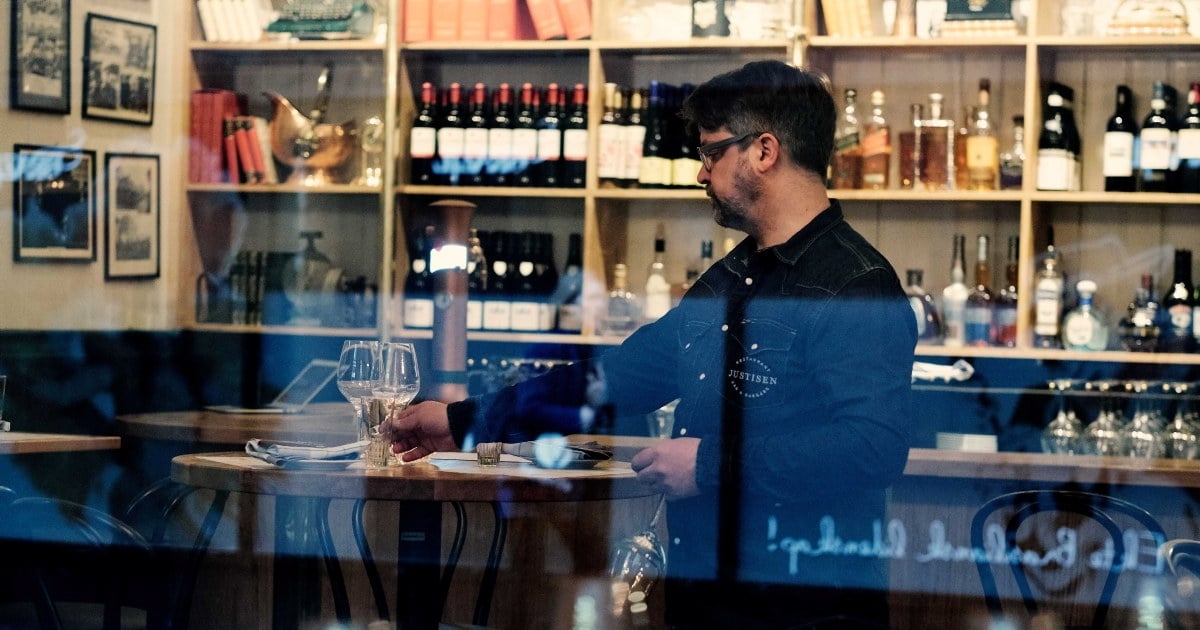 En ansatt som dekker et bord med glass i baren. Foto.