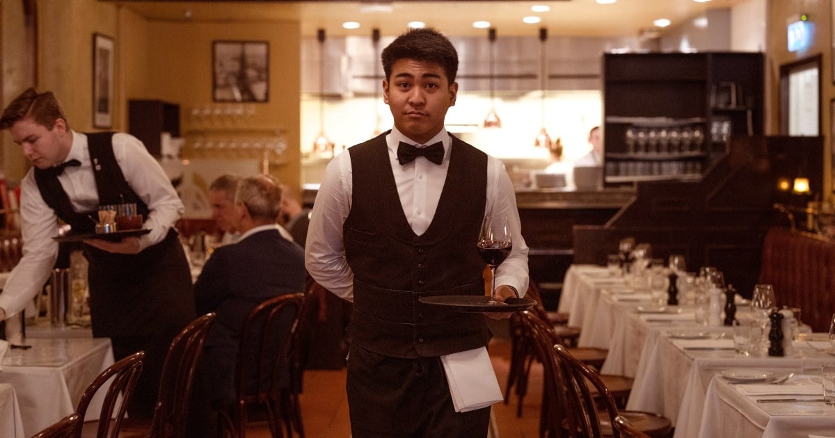 ung servitør som bærer et brett med et glass vin, i en restaurant.