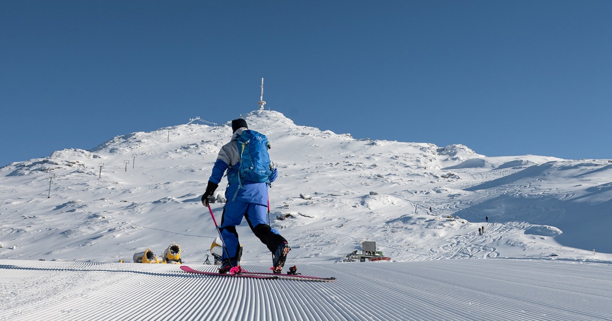 Preppet skiløype i forgrunnen. Person i blå dress som står på ski i bakgrunnen.