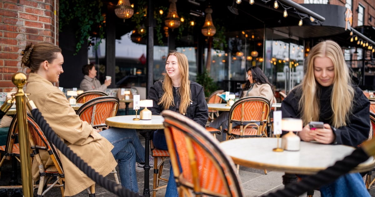 Gjester i uteserveringen til Pastis bistrobar på Aker brygge, med oransje bistrostoler og lyslenker.