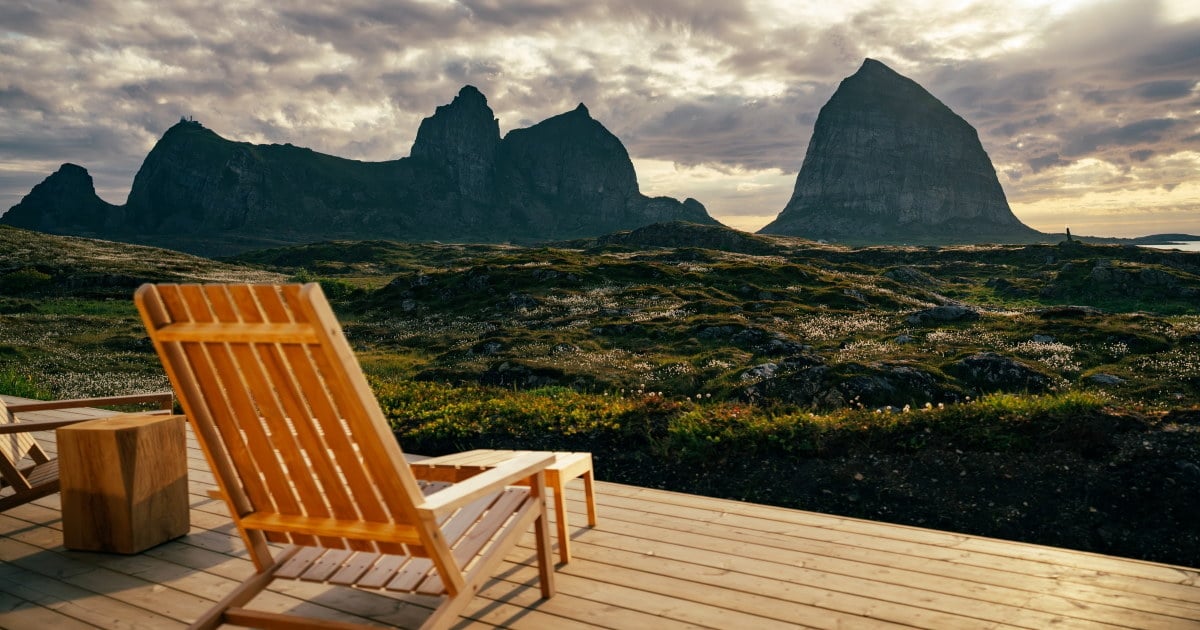 Treterrasse med stol foran et grønt kystlandskap og markante fjell på Træna. Foto.