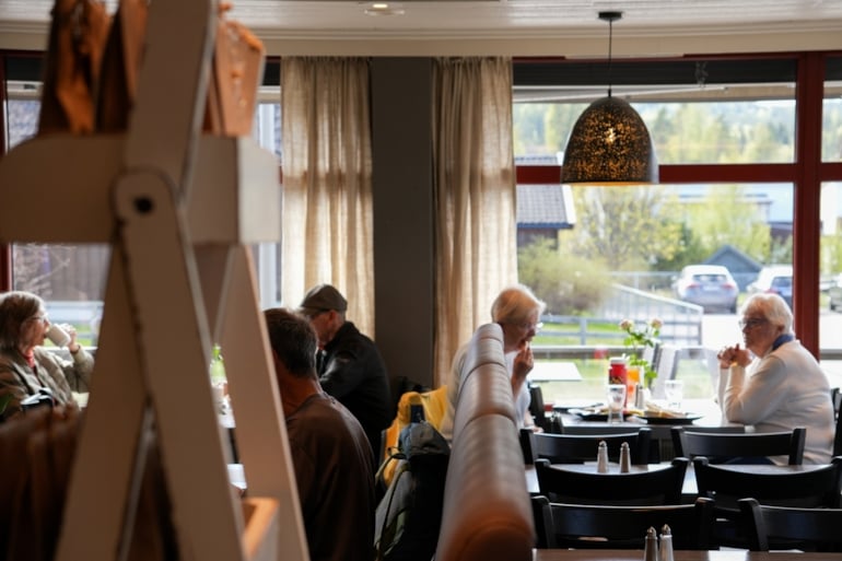 Gjester sitter ved bord inne i et serveringslokale.