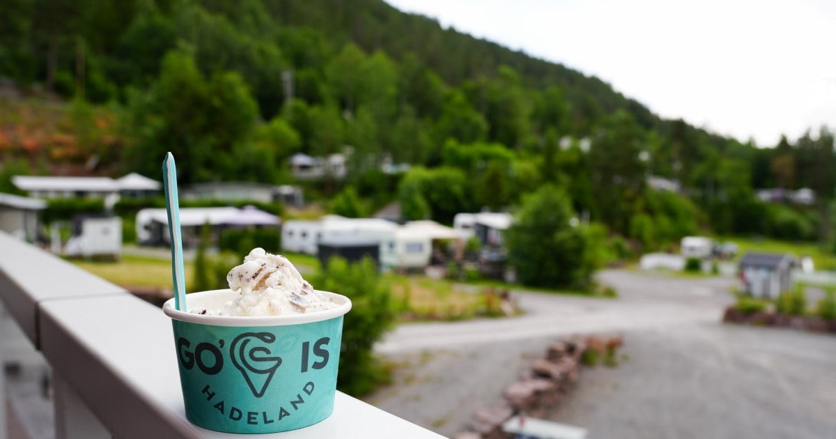 Et beger med iskrem står på et rekkverk, med campingvogner og en skogkledd ås i bakgrunnen.