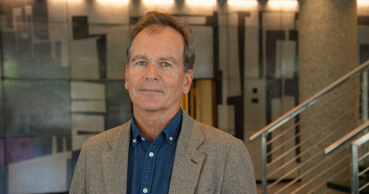 En person med grå blazer og mørkeblå skjorte ser mot kamera.