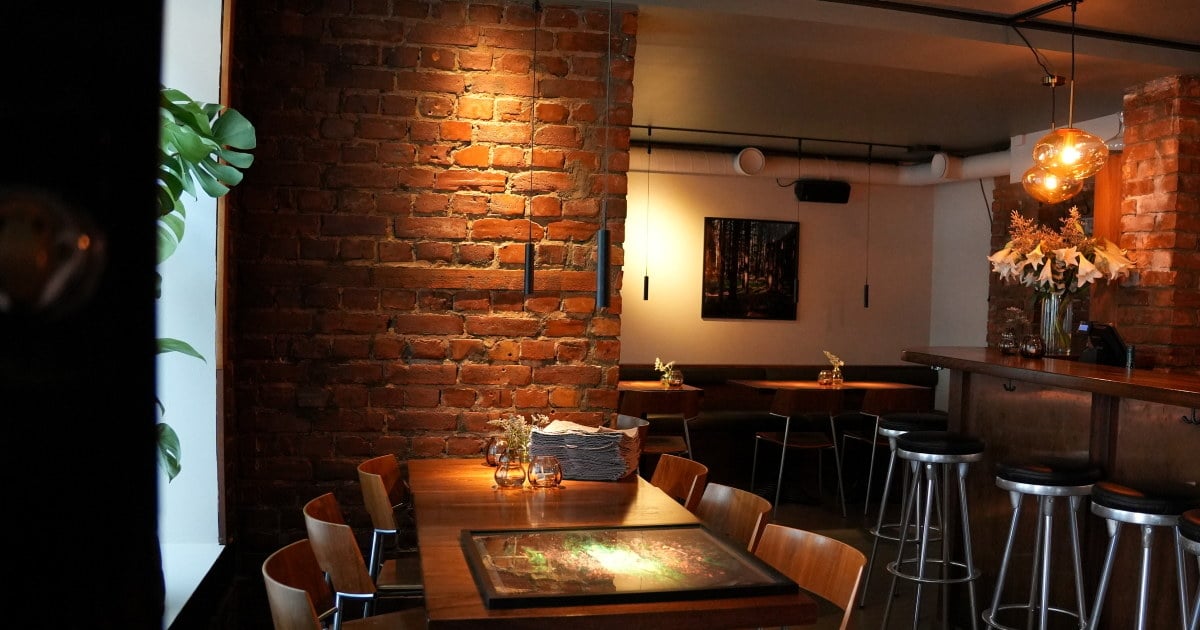 Restaurantlokale med bord, stoler, bardisk og murvegger.