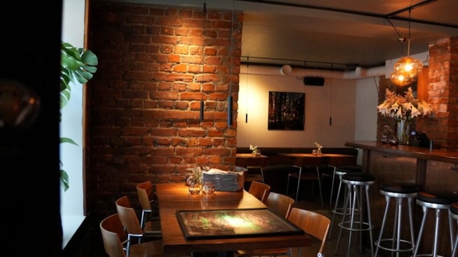 Restaurantlokale med bord, stoler, bardisk og murvegger.