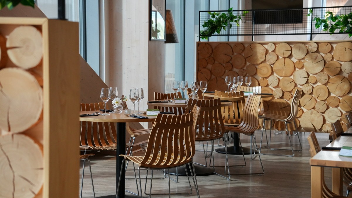Restaurantlokale med trebord, trestoler, dekkede bord og skillevegger med tverrsnitt av trestammer.