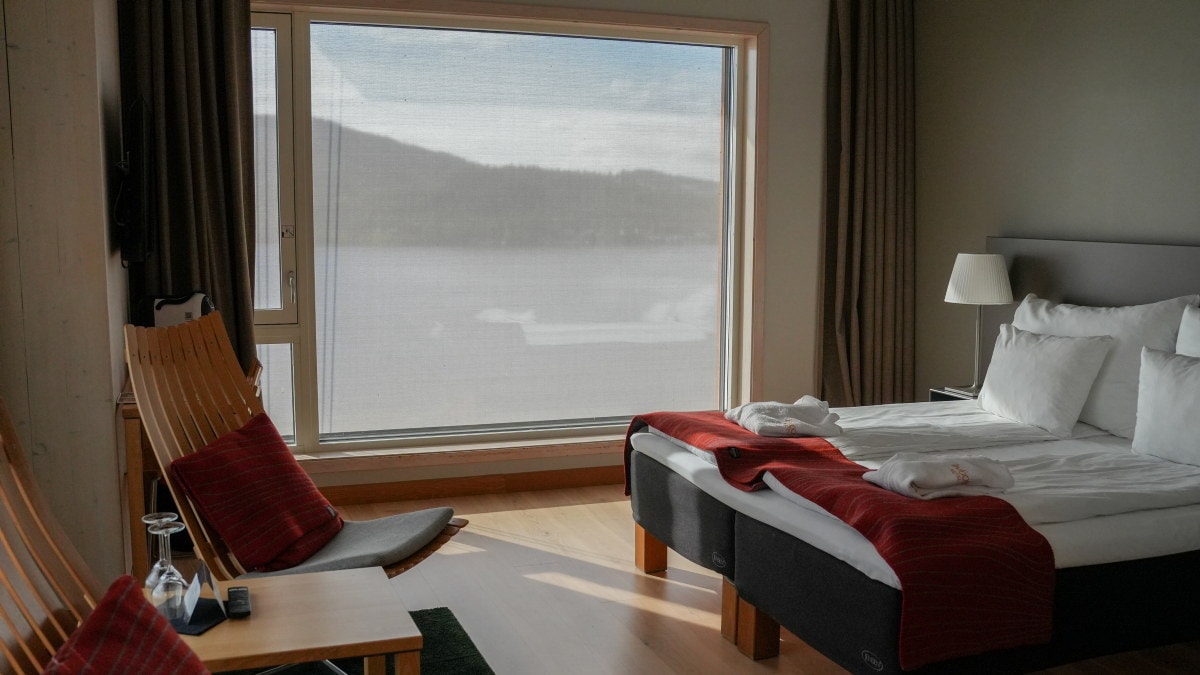 Hotellrom med dobbeltseng, to stoler, bord og stort vindu.