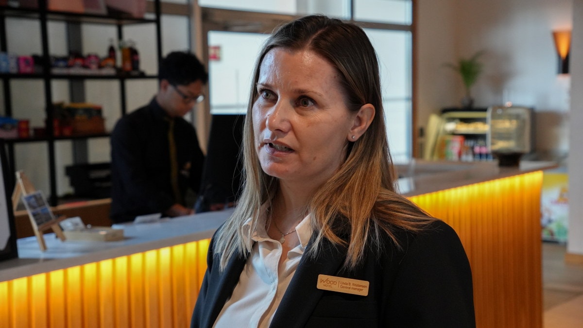 En person står foran en resepsjonsdisk. En annen person er synlig i bakgrunnen.