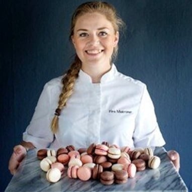 Smilende baker i arbeidsklær som holder et brett makroner