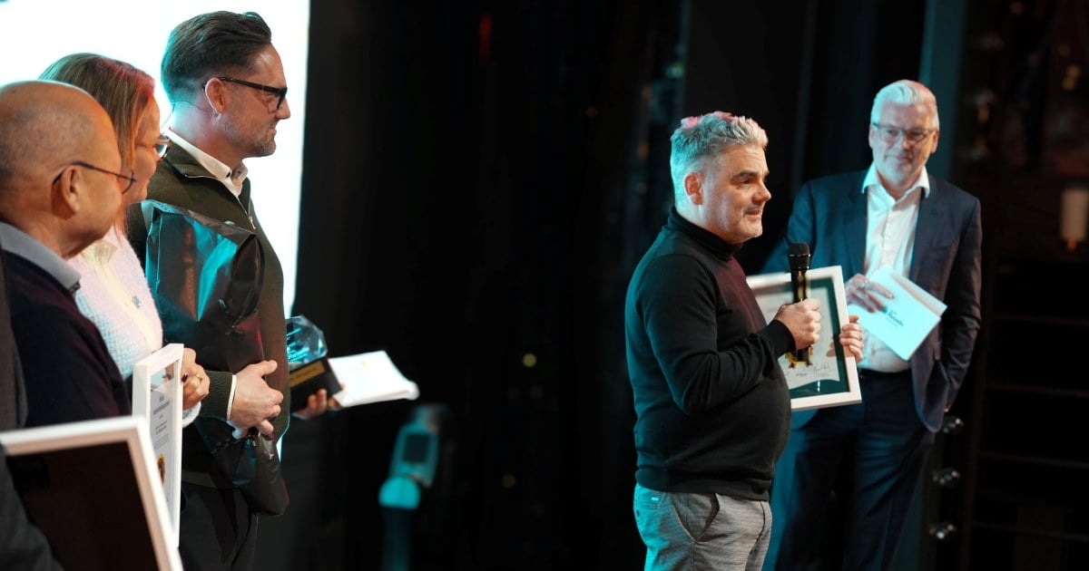 Prismottaker holder takketale med mikrofon blant flere mennesker på scenen under prisutdeling