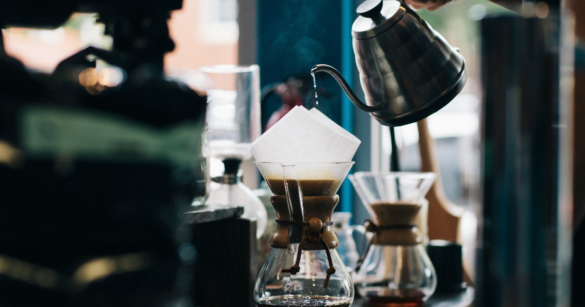 Utsnitt av hånd som heller varmt vann over i kaffeutstyr i grønne omgivelser