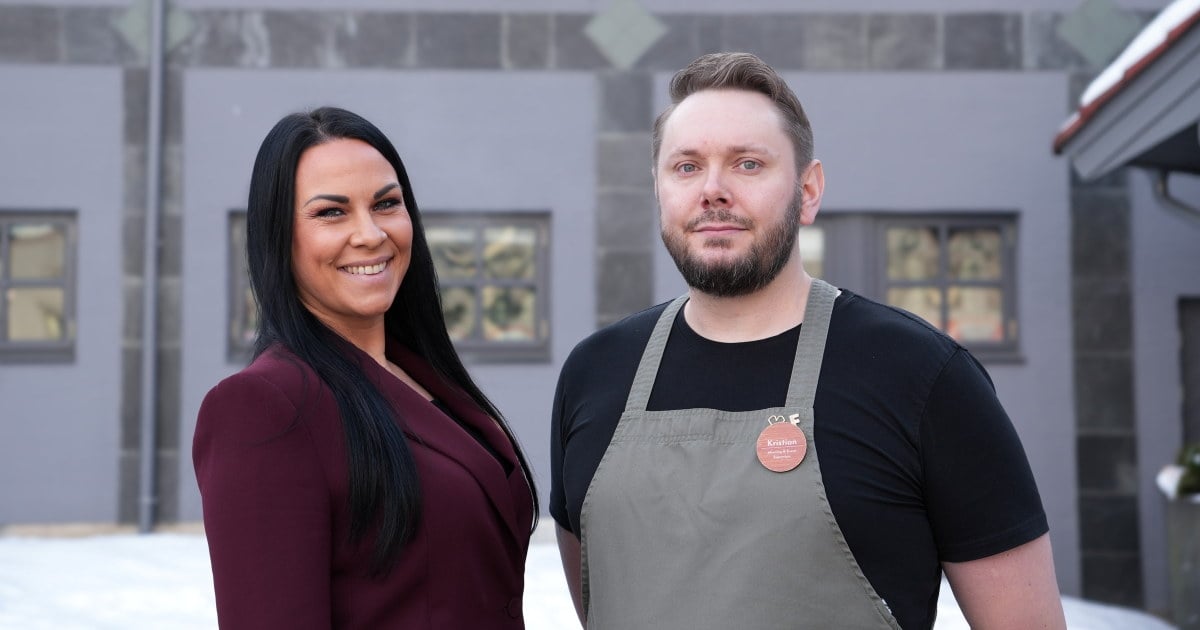 To personer står foran et hotellbygg og smiler til kamera.