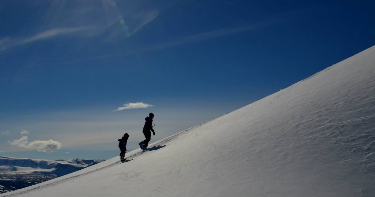 To personer som går opp en snødekket fjellside. Foto