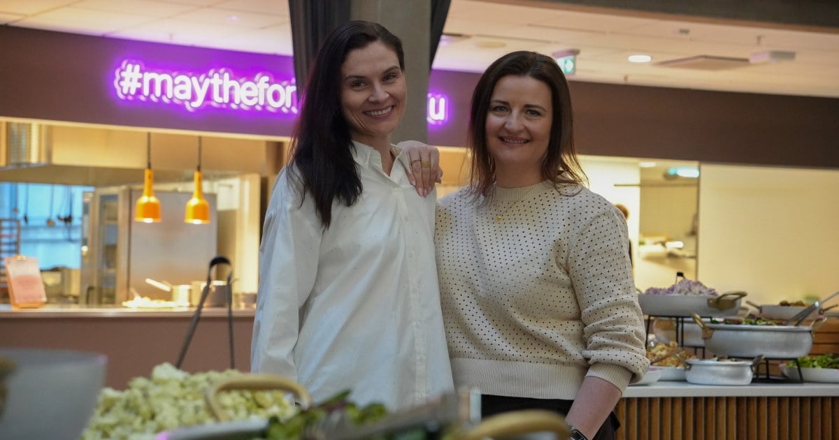 To personer smiler ved siden av buffet med ulike retter i kantine.