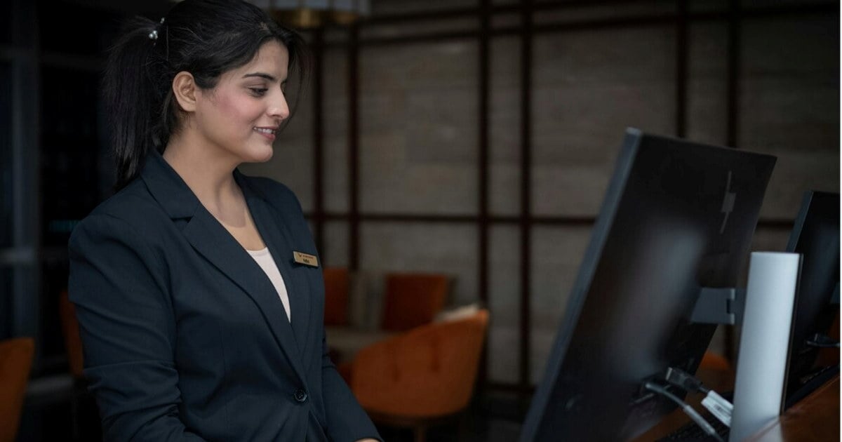 en hotellansatt som står bak en resepsjonsdisk.