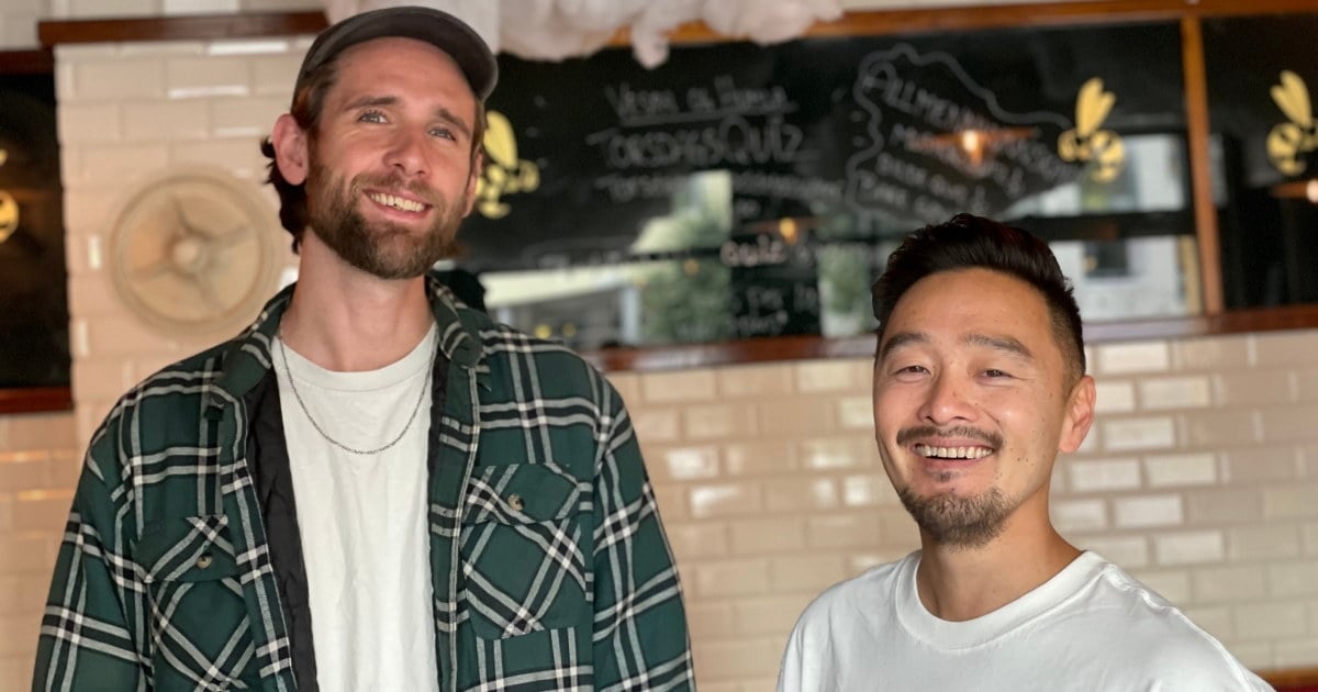 To menn smilende til kamera med restaurant i bakgrunnen