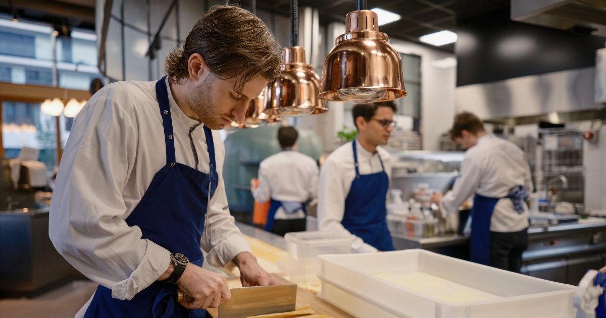 Kokk arbeider ved kjøkkenbenk og forbereder mat i profesjonelt restaurantkjøkken.