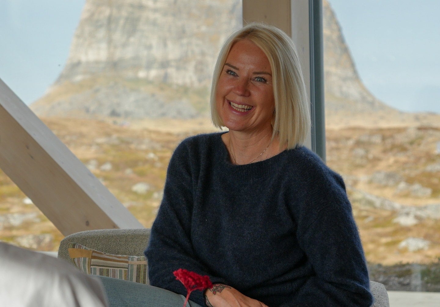 To personer sitter overfor hverandre og smiler, med fjell og natur synlig gjennom vinduet.