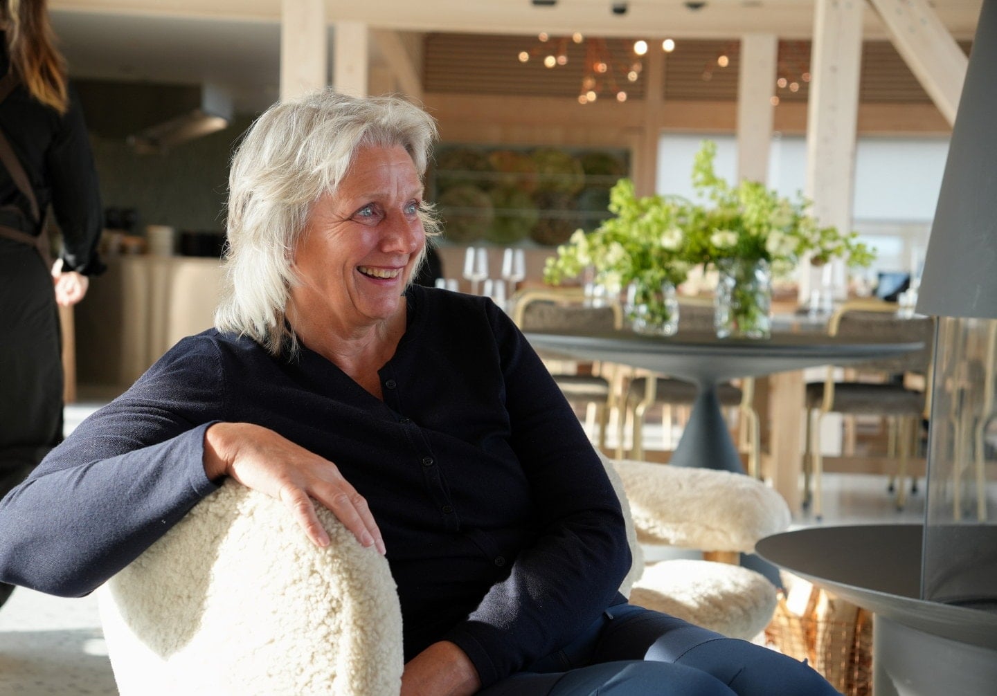 En person sitter i en lys lenestol og smiler under en samtale.