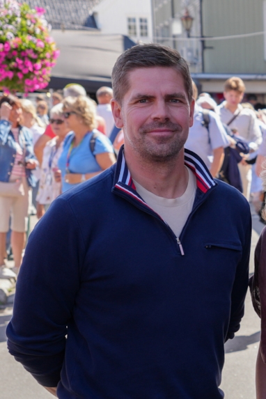 En person står med hendene bak ryggen og smiler til kamera.