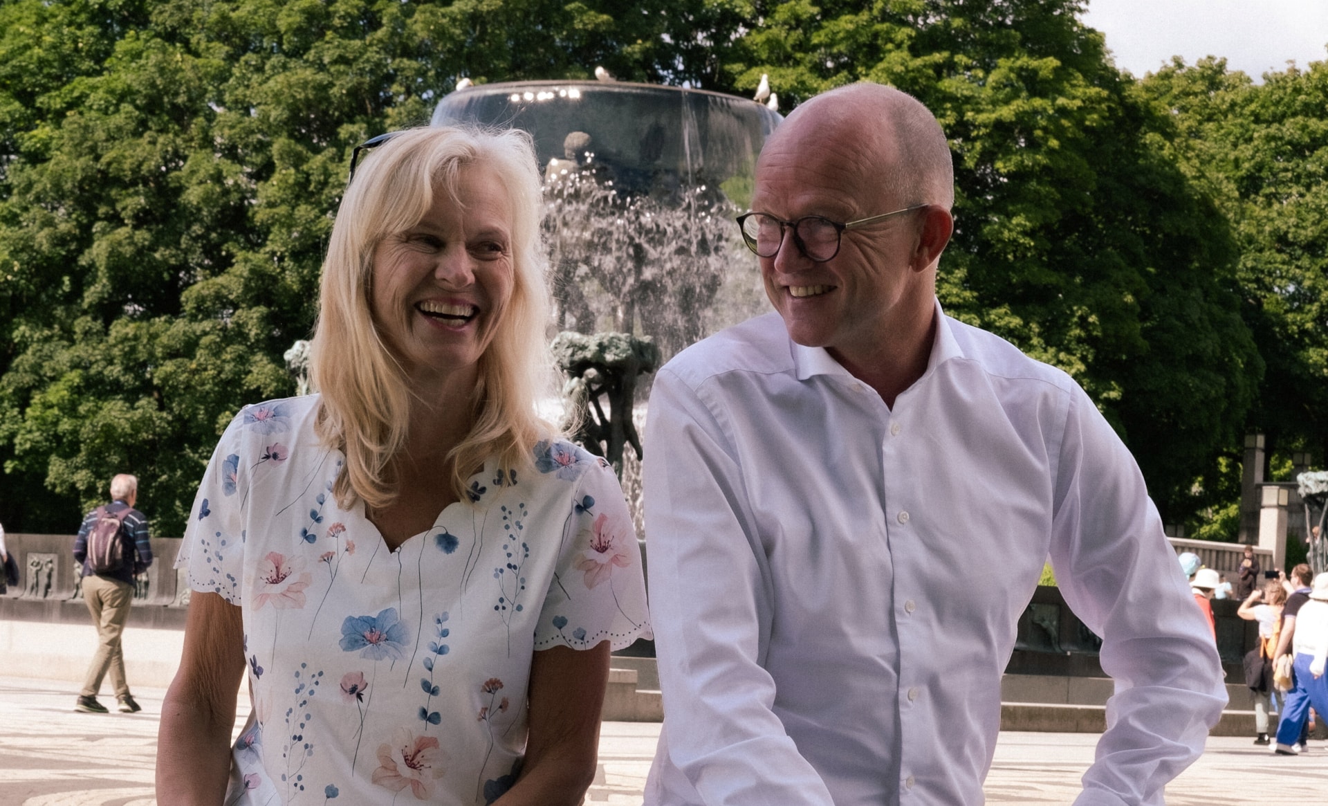 En kvinne og en mann som sitter og ler på en mur foran fontenen i Frognerparken. Foto