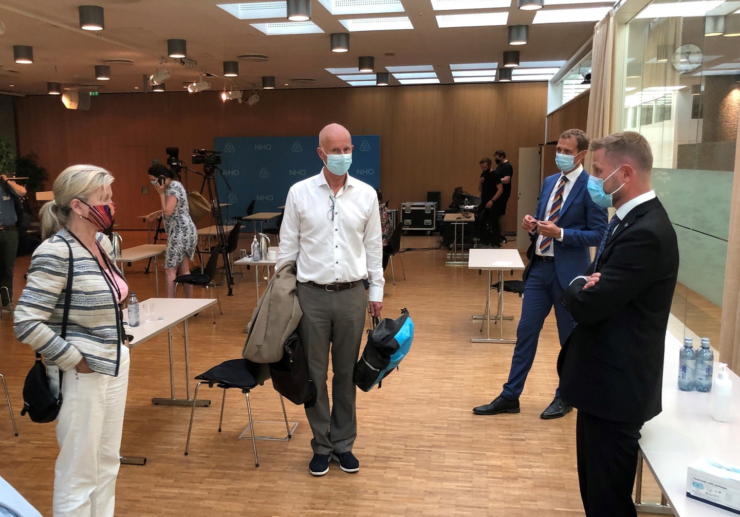 Tre menn og en kvinne som har på seg munnbind som står og har en samtale. Foto.
