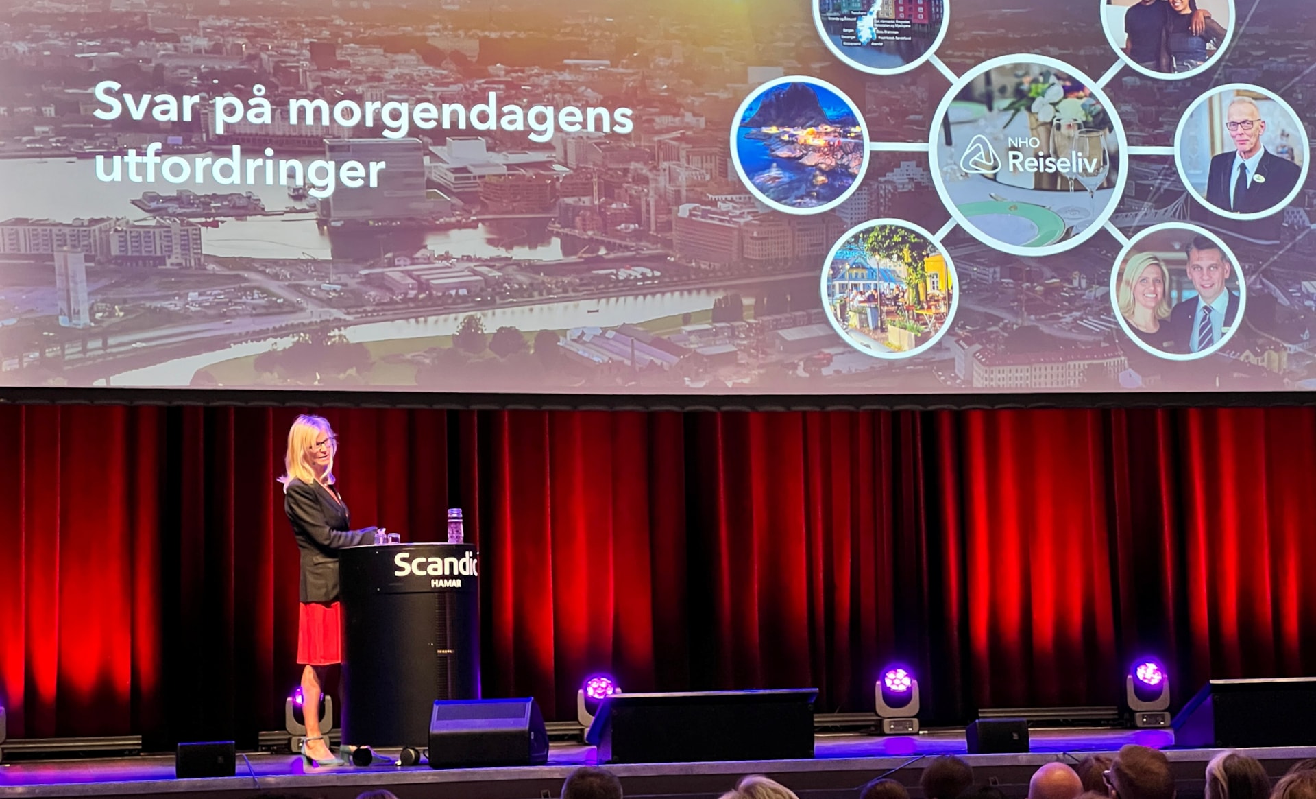 En kvinne i dressjakke og rød kjole som står på en scene. Foto