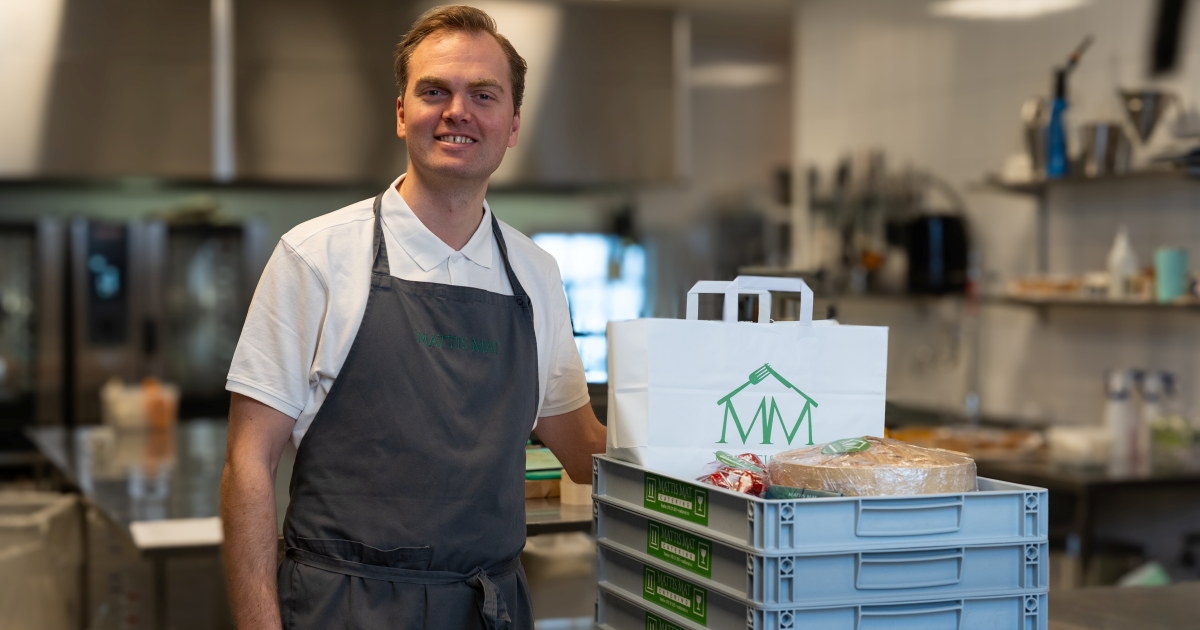 Kokk smiler til kamera ved siden av kasser med mat