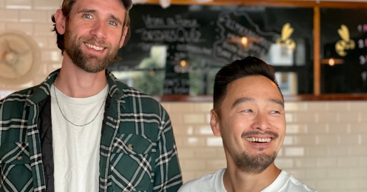 To menn smilende til kamera med restaurant i bakgrunnen