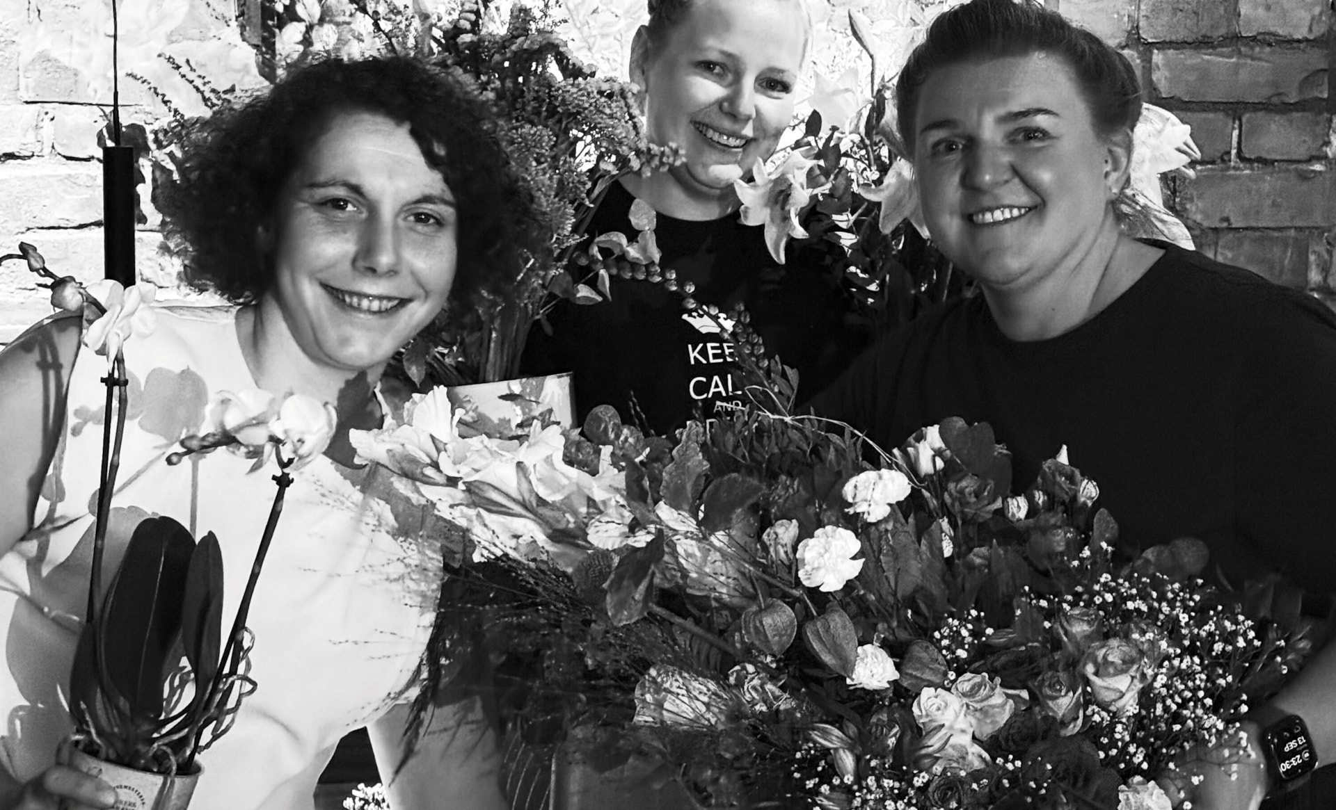 Svart-hvitt-bilde av tre personer som står sammen med flere blomsterbuketter og planter.