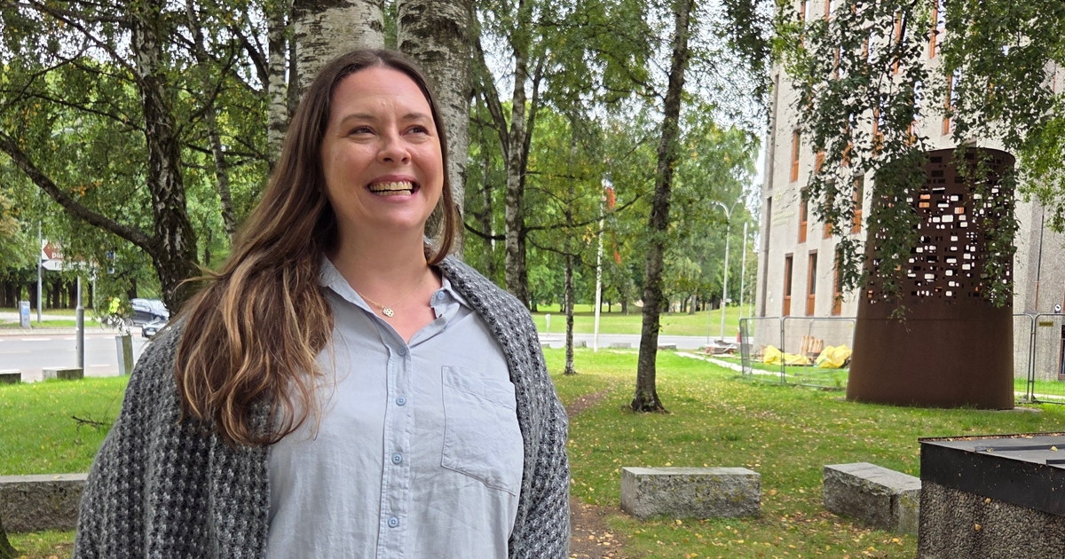 Kvinne ser i kamera med parknatur i bakgrunnen
