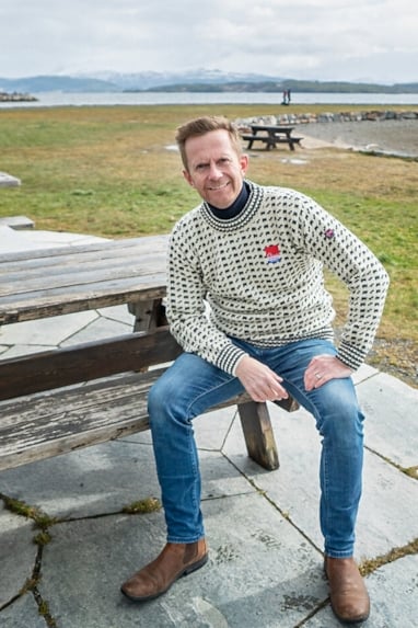 En blid mann som sitter på en benk og smiler til kameraet. Foto.