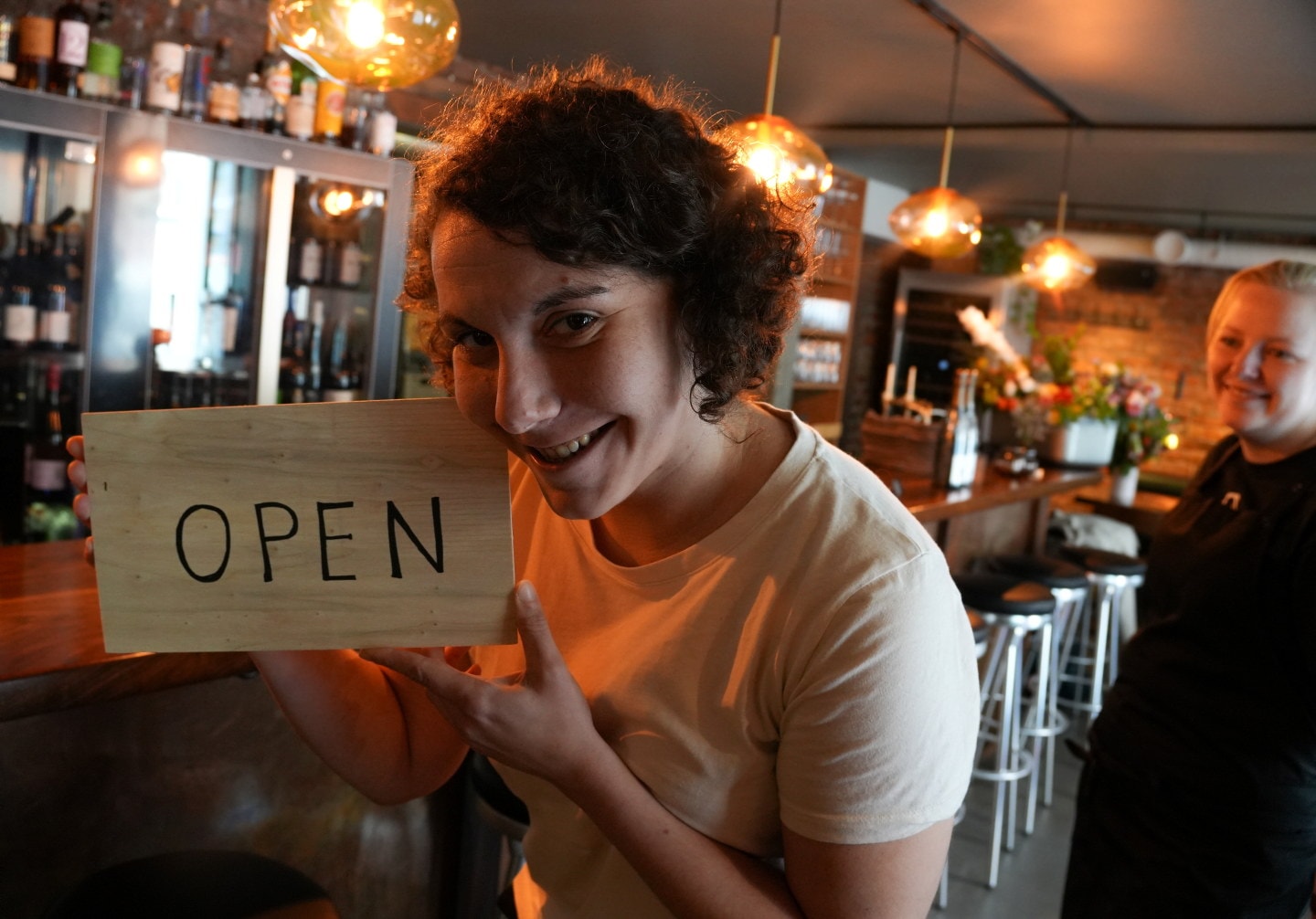 En person holder et skilt med teksten «OPEN» inne i en restaurant.