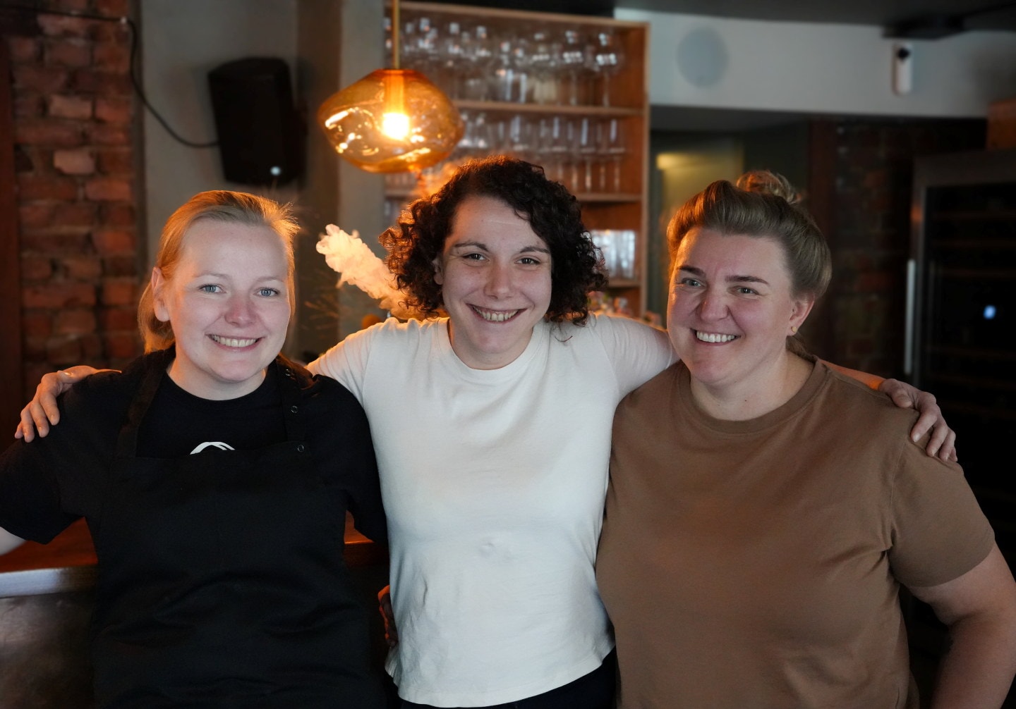Tre personer står sammen inne i et restaurantlokale.
