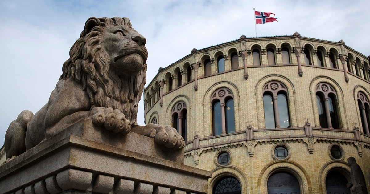 En løvestatue med Stortinget i bakgrunnen. Det norske flagget vaier fra toppen av Stortinget. Foto