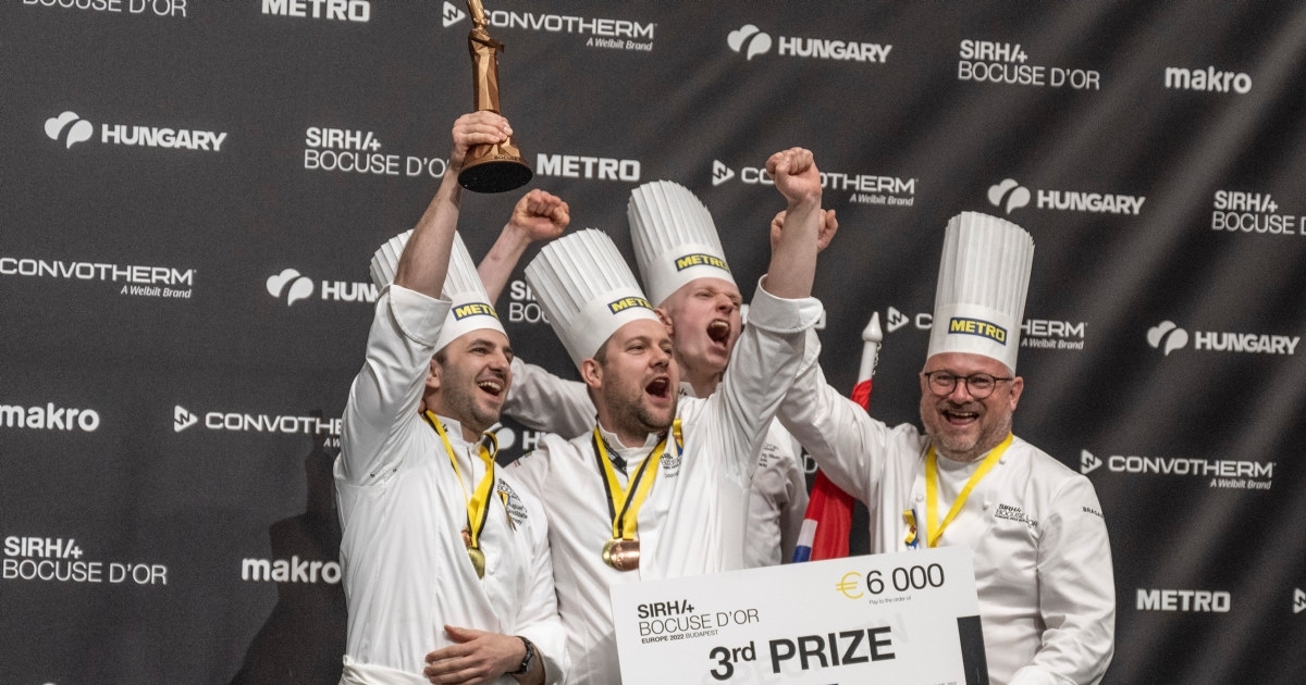 Fire jublende kokker med medaljer rundt halsen som holder en gavesjekk på 600 euro, og en Bocuse-statuett i bronse høyt hevet. Foto.