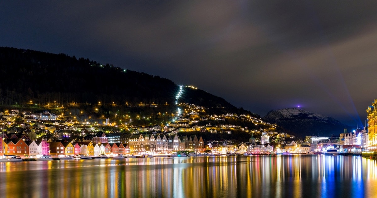 Nattbilde der lys fra bygninger reflekteres i vannet. Foto