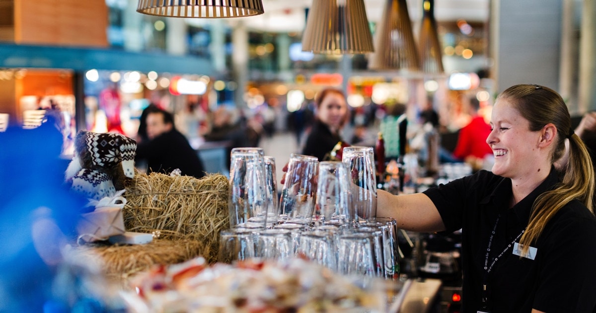 En servitør som stabler ølglass i baren. Foto.