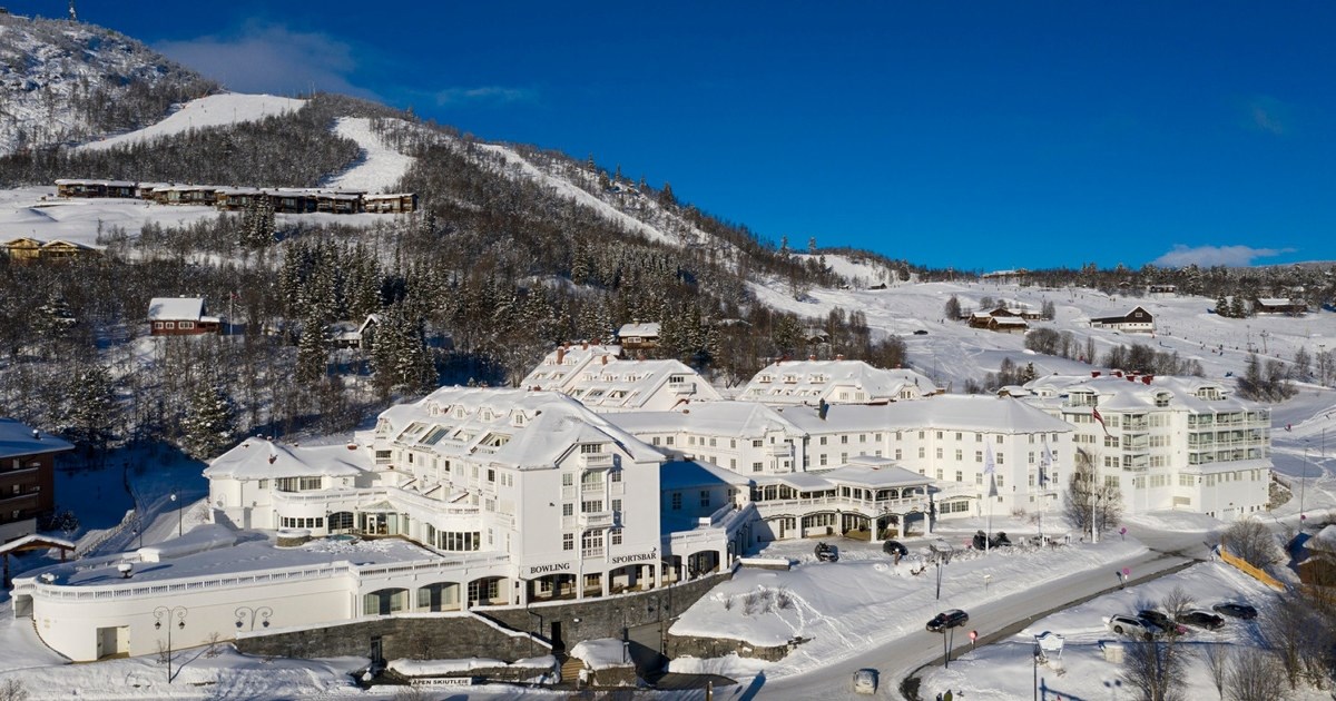 Bilde av et stort hvitt hotell, med skibakker, snø og blå himmel rundt.
