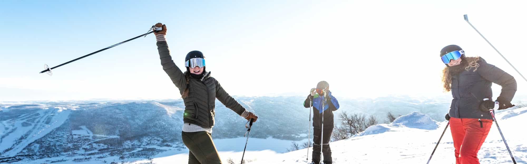 tre mennesker med slalåmski på beina med vakkert vinterlandskap i bakgrunnen. Foto