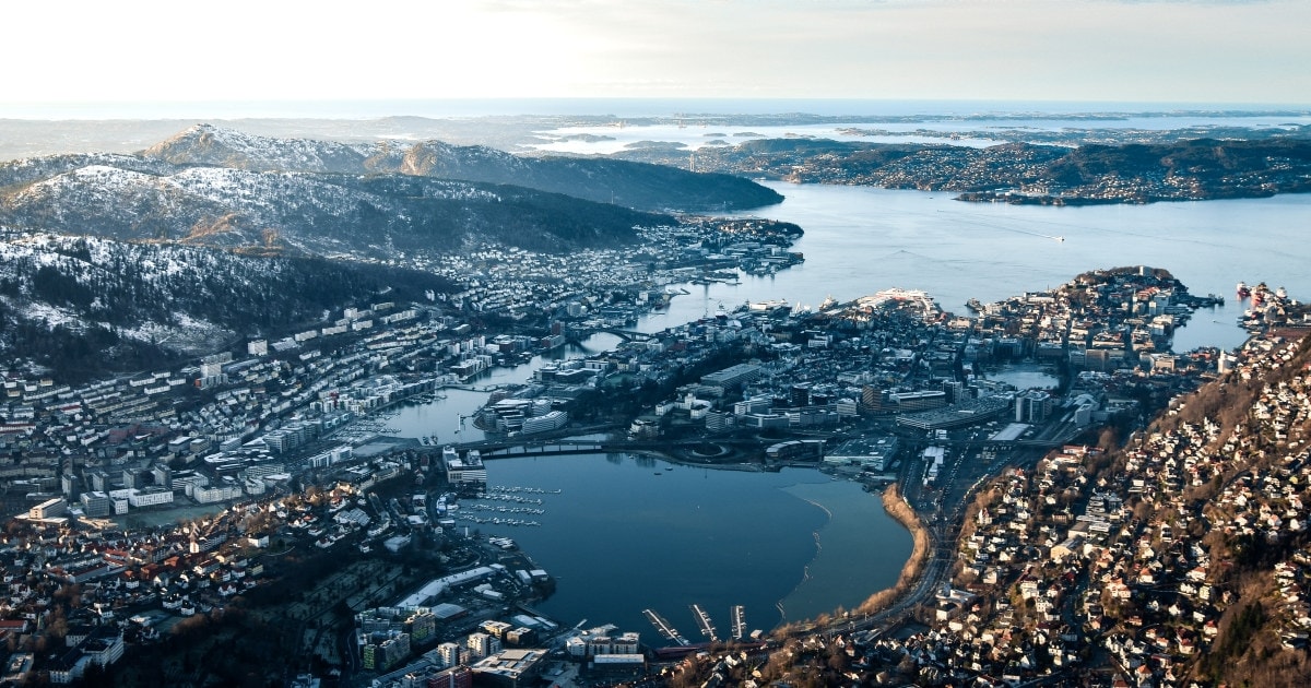 En by med vann, hus og fjell om vinteren sett ovenfra. Foto.