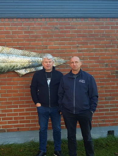 Daglig leder Tore Hamre og Salg- og markedssjef Thomas Hegge i Norice Seafood står utenfor hovedkontor med fisk på veggen i bakgrunnen.