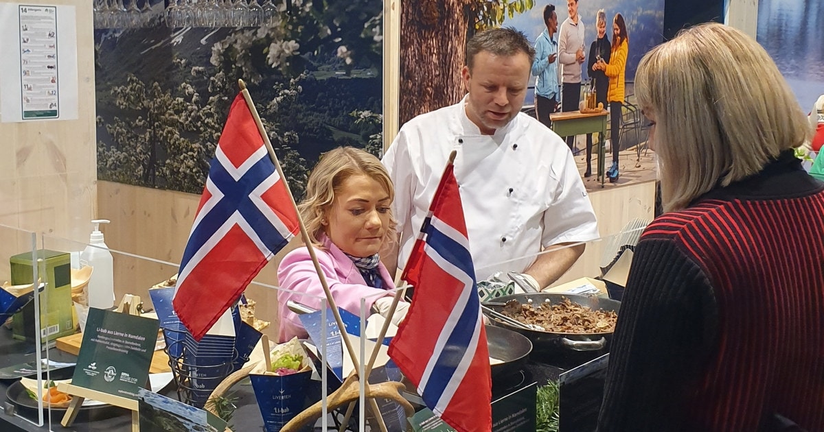 2 personer som står på bak en matstasjon og kokkelerer, men det norske flagget foran dem.